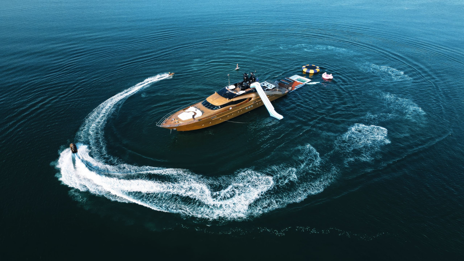 Gold superyacht at anchor on open water with water toys deployed